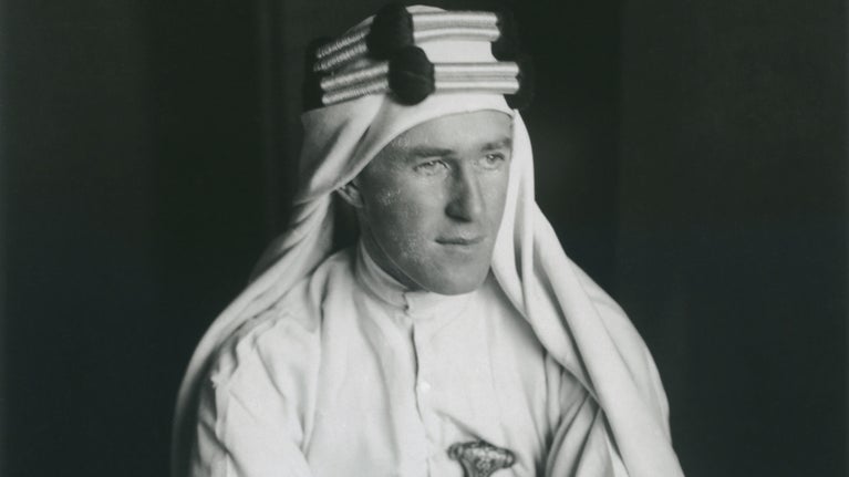Black and white portrait photograph of T. E. Lawrence dressed in Arabian style clothing.